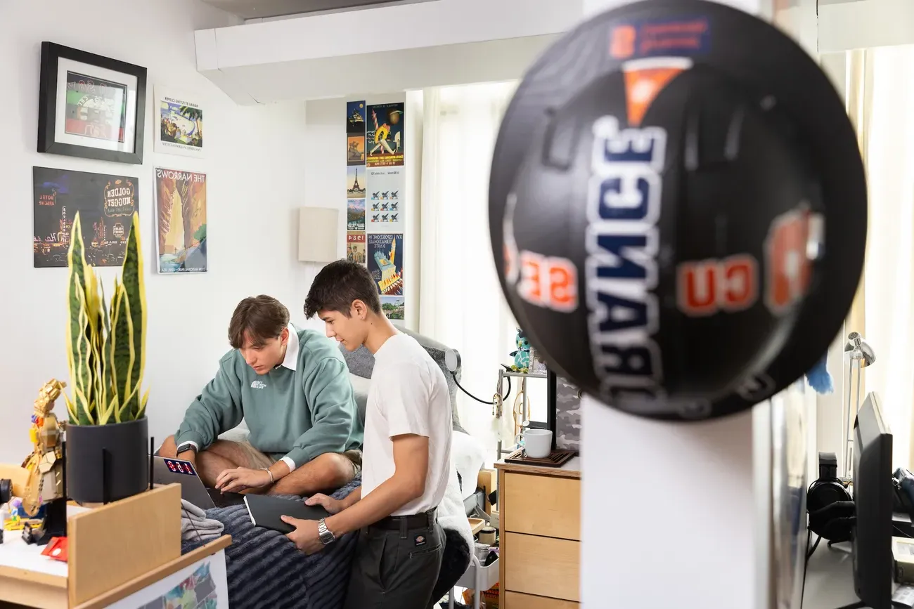 Two students sitting on bed and working in dorm room.